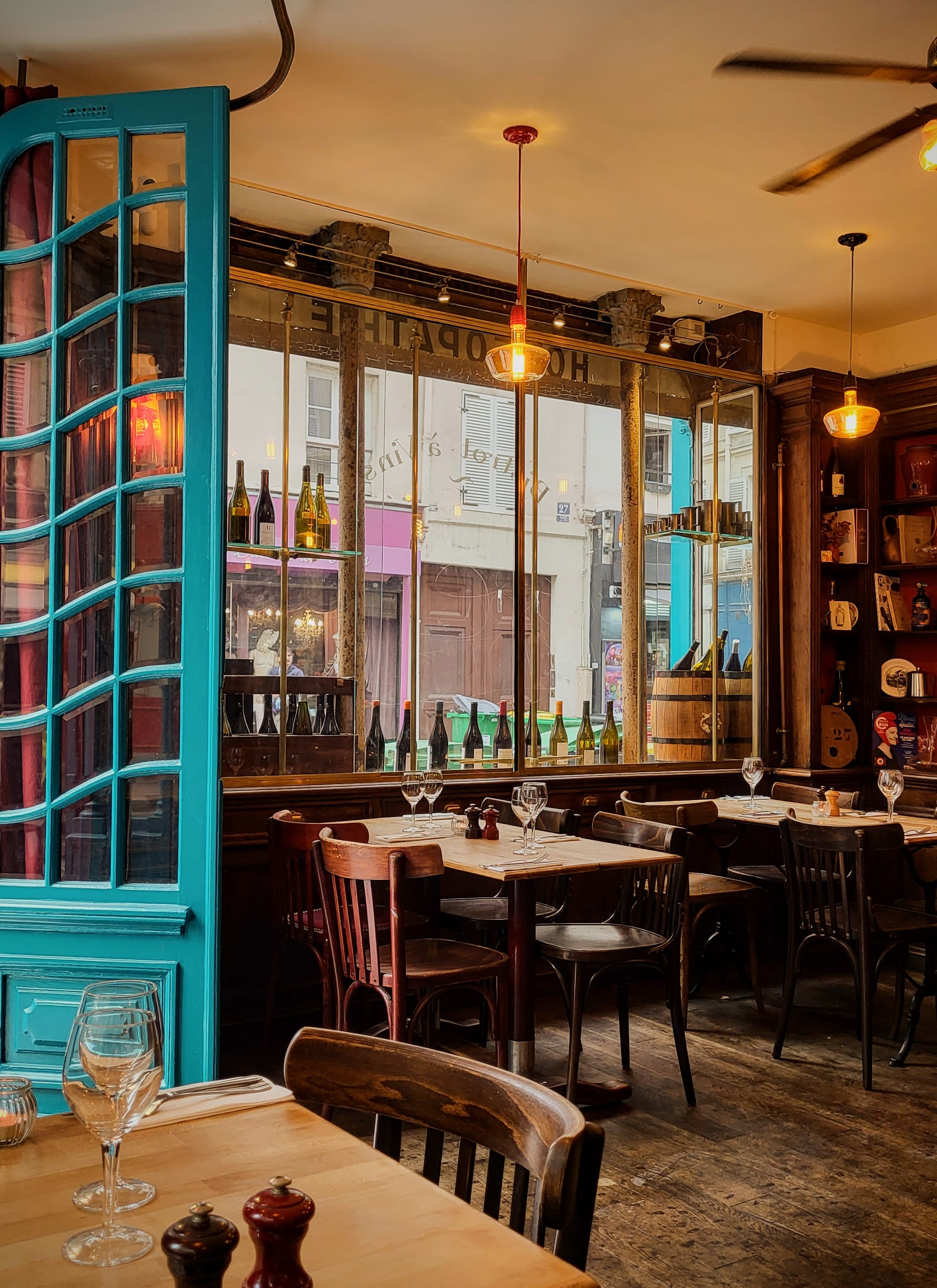 Salle chaleureuse de L'Officine Paris avec porte turquoise et tables de bistrot
